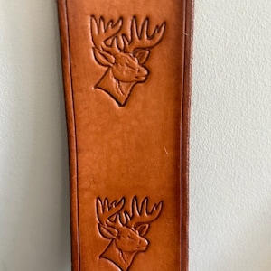 May include: A brown leather strap with two embossed deer head designs.