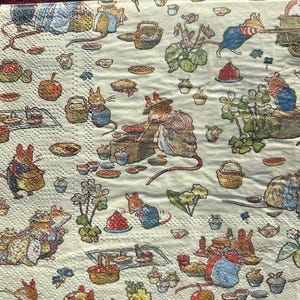 May include: A white paper napkin featuring a colourful illustration of mice and other woodland creatures enjoying a picnic. The design includes a variety of details, such as baskets, food, flowers, and trees.