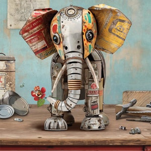 Peut inclure: Une sculpture d'éléphant en métal fantaisiste réalisée à partir de matériaux recyclés. L'éléphant est peint dans des tons de rouge, jaune, vert et bleu. La trompe de l'éléphant est étendue et tient une petite fleur rouge. La sculpture est posée sur un établi en bois avec un tiroir étiqueté "Metal Scraps (recycled)".