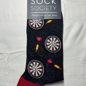 May include: Black socks featuring dartboard, dart, and heart designs. The socks have a red toe and heel. The tag reads "ONE SIZE FITS MOST" and "SOCK SOCIETY There's no secret here."