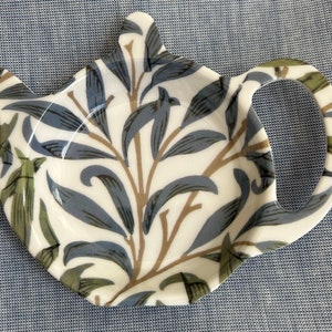 May include: White ceramic teapot cosy with a blue and green floral pattern. The cosy has a handle shaped like a teapot spout.