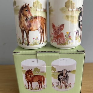 May include: A set of salt and pepper shakers in a white box with a green lid. The shakers are ceramic and feature farm animal illustrations. The front of the box says "Salt & Pepper".