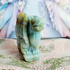 May include: A carved stone dragon figurine in shades of blue, green, and yellow. The dragon has detailed wings, scales, and a fierce expression. The figurine is a decorative item, possibly for display or collection.