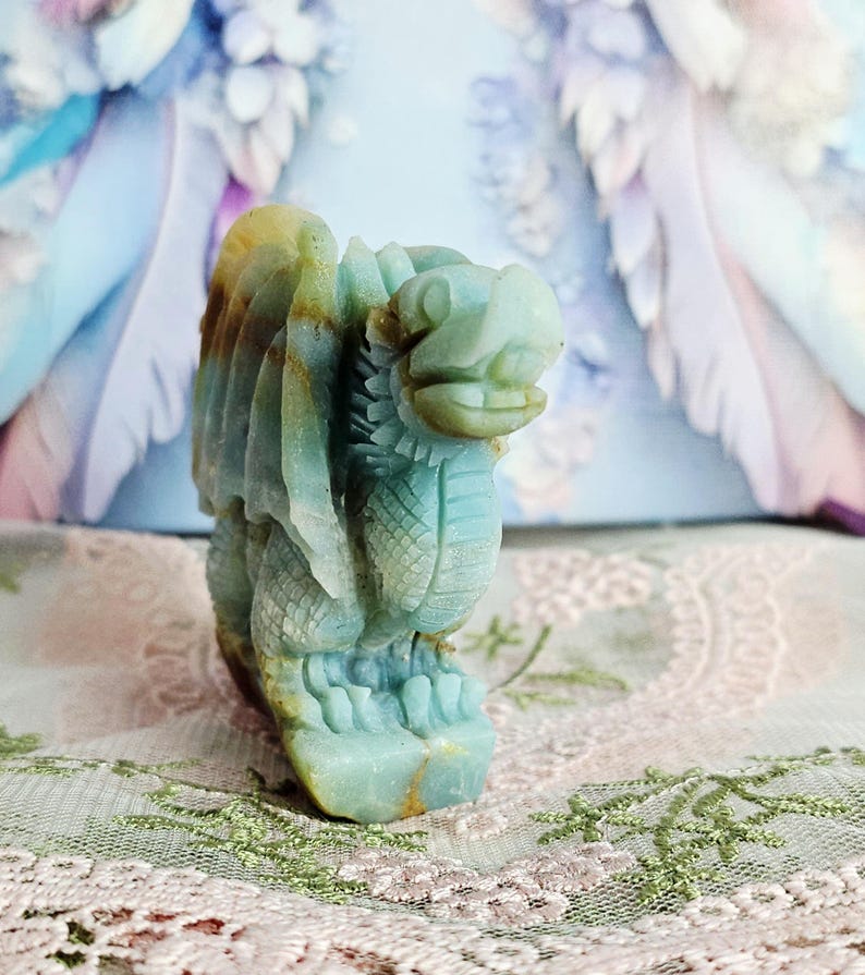 May include: A carved stone dragon figurine in shades of blue, green, and yellow. The dragon has detailed wings, scales, and a fierce expression. The figurine is a decorative item, possibly for display or collection.