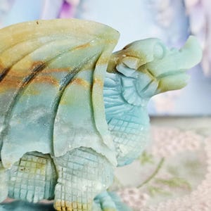 May include: A carved stone dragon figurine in shades of blue, green, and brown. The dragon has detailed wings, scales, and a textured body. The sculpture is a decorative item, possibly for display or collection.