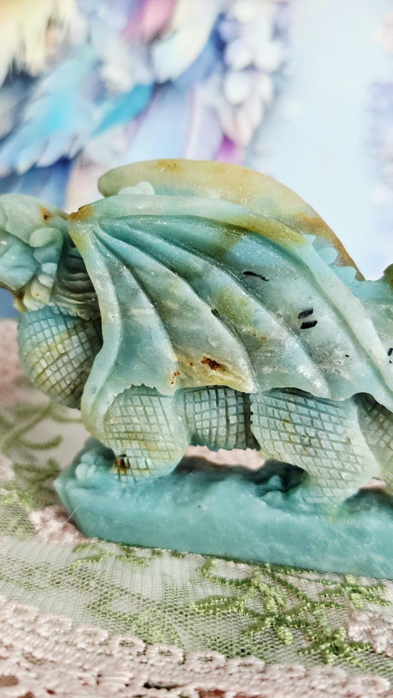 May include: A detailed, close-up of a turquoise dragon sculpture. The dragon has textured wings and scales, with hints of brown and yellow. The sculpture is set against a soft, blurred background.