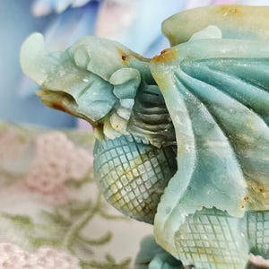 May include: A detailed sculpture of a dragon in shades of blue and green. The dragon has intricate carved details, including scales, wings, and a textured body. The sculpture is set against a soft, blurred background.