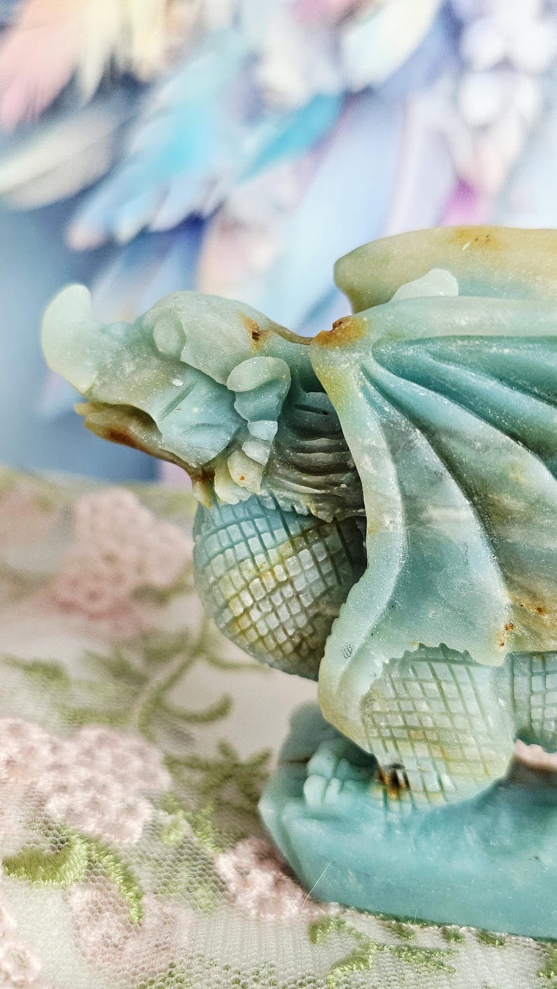 May include: A detailed sculpture of a dragon in shades of blue and green. The dragon has intricate carved details, including scales, wings, and a textured body. The sculpture is set against a soft, blurred background.