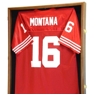 May include: A red football jersey with white numbers and the name "MONTANA" on the back. The jersey is displayed in a wooden shadow box with a black background.