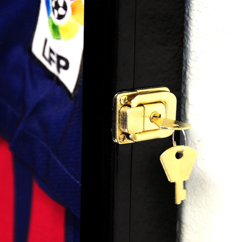 May include: A black wooden display case with a gold lock and key. The case has a clear glass front and is designed to hold and display a jersey or other sports memorabilia.