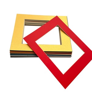 May include: A stack of colourful mat boards with a red mat board on top. The mat boards have a white core and a coloured outer layer. The mat boards are used for framing pictures and artwork.