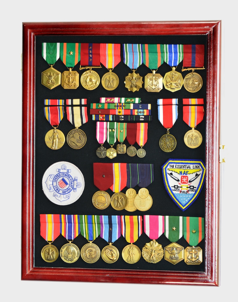 May include: A mahogany wood shadow box display case with a black felt background. The case is filled with military medals, ribbons, and patches. The medals are gold and silver and feature various designs, including eagles, stars, and anchors. The ribbons are red, white, blue, and green. The patches are embroidered with the words "The Essential Link" and "NAF" and feature a plane and a cross.