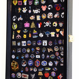 May include: Black shadow box display case filled with a variety of colorful enamel pins. The pins feature cartoon characters, logos, and other designs.