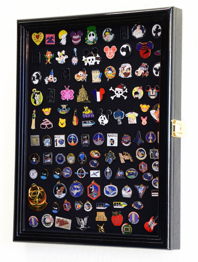 May include: Black shadow box display case filled with a variety of colorful enamel pins. The pins feature cartoon characters, logos, and other designs.