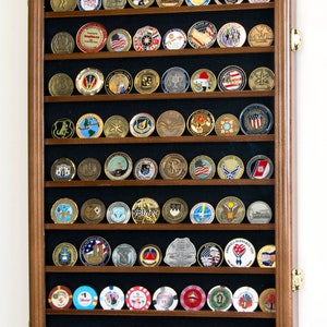 May include: A wooden shadow box display case with 10 rows of slots for displaying coins or challenge coins. The case has a dark brown wood frame and a black felt backing. The case is filled with a variety of coins, including casino chips, military challenge coins, and other commemorative coins.