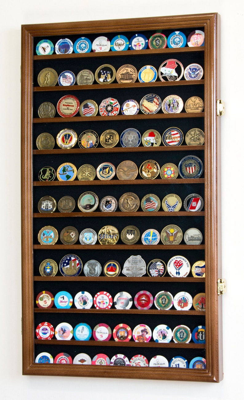 May include: A wooden shadow box display case with 10 rows of slots for displaying coins or challenge coins. The case has a dark brown wood frame and a black felt backing. The case is filled with a variety of coins, including casino chips, military challenge coins, and other commemorative coins.