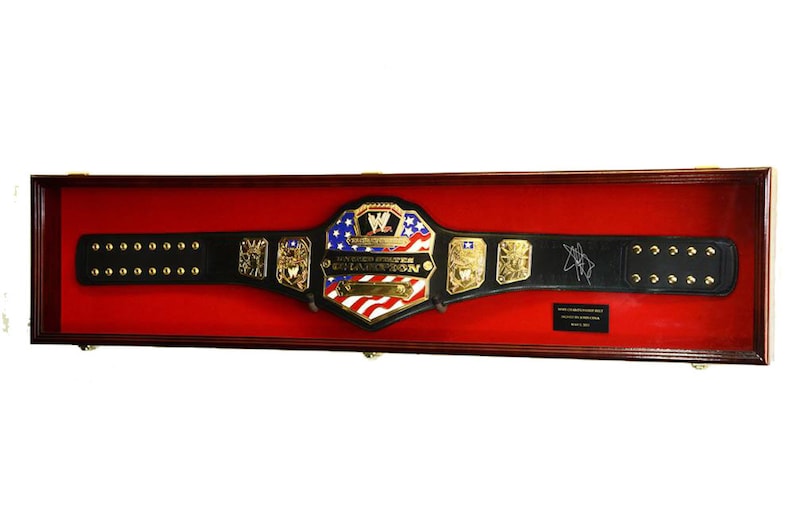 May include: A black leather wrestling championship belt with gold accents and a red, white, and blue American flag design. The belt is displayed in a wooden shadow box with a red velvet lining. The belt is signed "The American Dream, Dusty Rhodes".