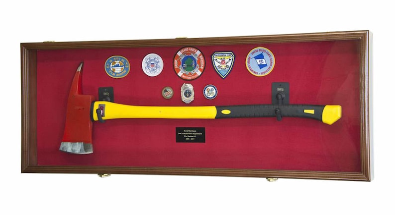 Pu&ograve; includere: Una scatola di ombra in legno con un rivestimento in feltro rosso mostra un'ascia da pompiere con un manico giallo e una testa nera. La scatola presenta anche diversi distintivi e spille, tra cui un emblema della Guardia Costiera e una toppa della Guardia Costiera Ausiliaria degli Stati Uniti.