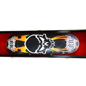 May include: Black skateboard display case with a red velvet interior. The skateboard has a black and orange design with a white skull graphic and the text "Ride or Die" on the bottom right corner.