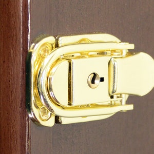 May include: A gold-toned metal latch with a keyhole. The latch is attached to a wooden surface.