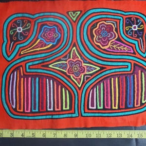 Puede incluir: Un textil mola colorido con un dise&ntilde;o geom&eacute;trico que presenta un motivo floral central y dos p&aacute;jaros a cada lado. El mola est&aacute; hecho de tela y est&aacute; cosido con hilos de colores.