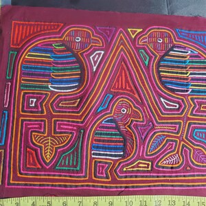 Puede incluir: Una obra de arte textil bordada de colores que representa tres p&aacute;jaros con dise&ntilde;os intrincados. Los p&aacute;jaros est&aacute;n delineados en negro y rellenos de colores vibrantes como rojo, azul, verde y amarillo. El fondo es de color burdeos oscuro.