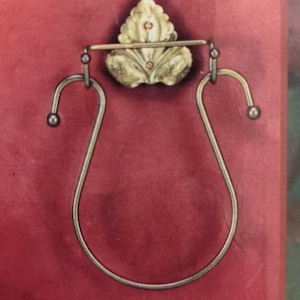 May include: A decorative metal towel ring with a leaf design. The ring is silver-toned with a curved shape and small ball accents. The background is a deep red colour.