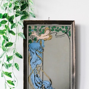 Könnte beinhalten: Gerahmter Spiegel mit Jugendstil-Design. Die Illustration zeigt eine Frau in einem blauen Kleid mit blonden Haaren, umgeben von Weinreben. Der Text "Moët & Chandon" ist sichtbar.