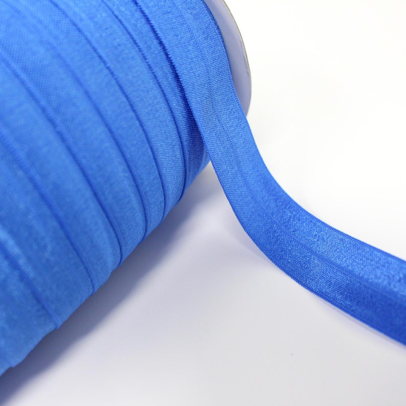 Op de afbeelding: Een rol helderblauw elastisch lint. Het lint is gevouwen en opgerold, met een klein deel van het lint uitgerold.