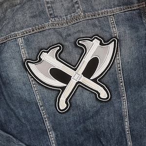 Puede incluir: Una chaqueta vaquera con un parche bordado en plata y negro de dos hachas cruzadas.