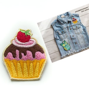 May include: Embroidered cupcake patch with pink frosting, chocolate icing, and a red strawberry on top. The patch is yellow and has a white outline. #EmbroideryPatch On Kids Jacket