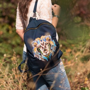 May include: A navy blue backpack with a colorful lion design on the front. The backpack has a zipper closure and a brown leather strap.