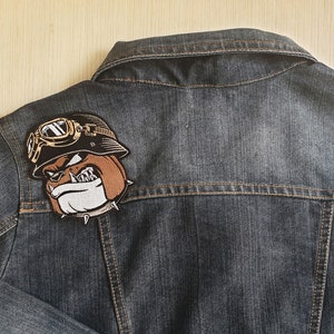 May include: A dark blue denim jacket with a brown and white embroidered patch of a bulldog wearing goggles and a helmet.