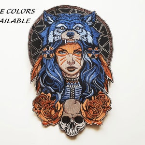Puede incluir: Parche bordado con una mujer con un tocado de cabeza de lobo, de color azul y naranja, y una calavera con rosas debajo. El texto "More Colors Available" es visible.