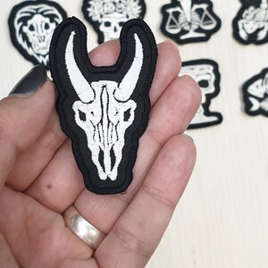 Op de afbeelding: Geborduurde zwart-witte patches met gotische en occulte ontwerpen. De belangrijkste patch is een witte stierschedel op een zwarte achtergrond. Andere patches zijn onder meer schedels, weegschalen en vissenskeletten. Ideaal om kleding of accessoires te personaliseren.