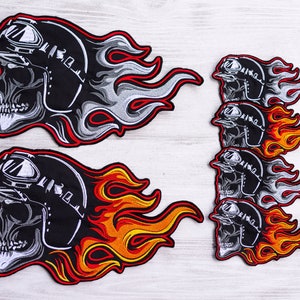 Könnte beinhalten: Gestickte Aufnäher mit einem Totenkopf, der einen Motorradhelm mit Brille trägt und von Flammen umgeben ist. Die Aufnäher sind schwarz, weiß, rot und orange. Die Aufnäher sind in verschiedenen Größen und Mengen.