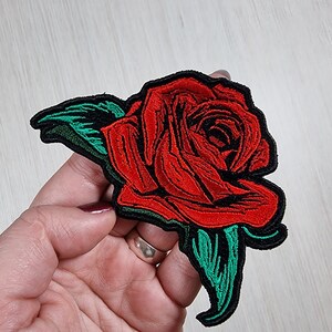 May include: Red embroidered rose patch with green leaves. The rose is a classic symbol of love and beauty.
