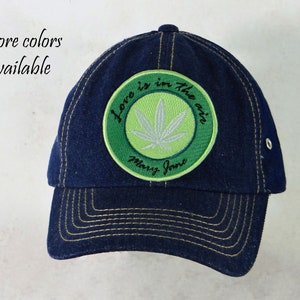Peut inclure: Une casquette de baseball en denim bleu foncé avec un patch brodé vert et blanc qui dit "Love is in the air, Mary Jane".