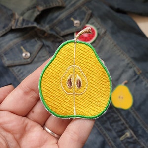May include: A yellow pear-shaped embroidered patch with a green outline and a brown seed detail. The patch is on a denim jacket.