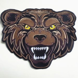May include: Embroidered patch featuring a detailed bear head with an aggressive expression. The patch showcases brown, black, and tan colors, with yellow eyes and sharp white teeth. The bear's fur is intricately stitched.