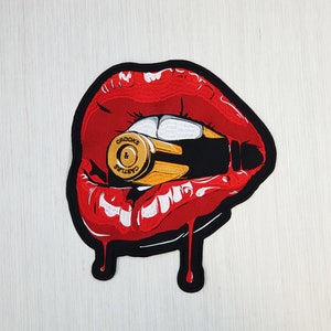 May include: Red lips with a bullet in the mouth. The bullet is gold and has the words "Crooks & Castles" on it.