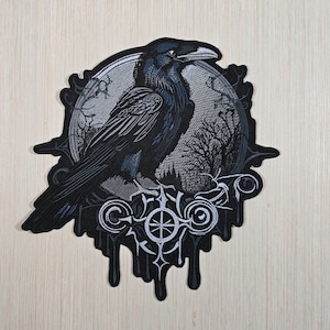 May include: A black and gray patch featuring a detailed illustration of a raven perched on a decorative emblem. The raven is depicted with intricate feather details, set against a backdrop of a forest and a circular design.