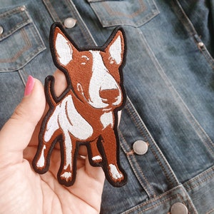May include: Brown and white embroidered patch of a bull terrier dog. The patch is on a denim jacket.