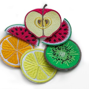 May include: Five embroidered fruit patches, including a red apple, a watermelon, a kiwi, an orange, and a lemon. The patches are arranged in a circle on a white background.