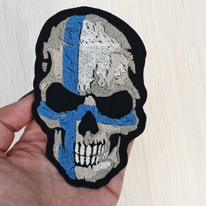 May include: Embroidered patch of a skull with a blue, white, and gray design. The skull is outlined in black.