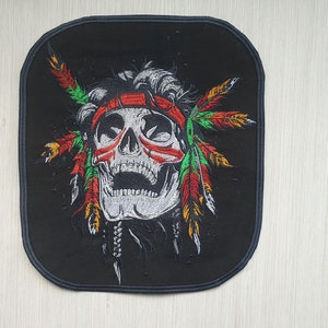 May include: Black embroidered patch featuring a white skull wearing a red, green and yellow headdress with feathers.
