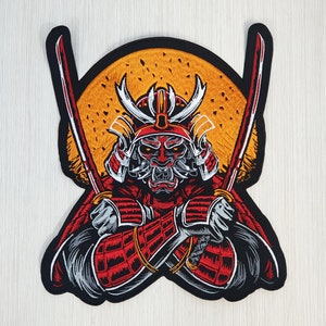 Puede incluir: Parche bordado con un guerrero samurái rojo y negro con espadas cruzadas, sobre un fondo de sol amarillo.