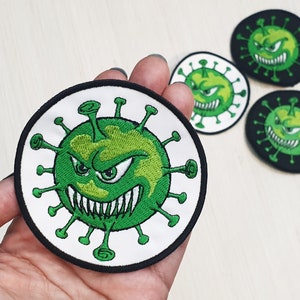 May include: Four embroidered patches featuring a green cartoon virus with a menacing expression and sharp teeth. The virus is surrounded by a white background and a black border.