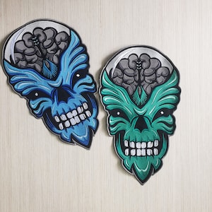 May include: Two embroidered patches featuring a skull with a brain visible inside. One patch is blue and the other is green.