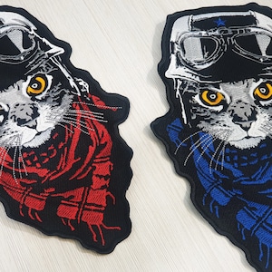Peut inclure: Deux patchs brodés thermocollants représentant un chat portant un casque en cuir et des lunettes. Un patch a une écharpe rouge et l'autre une écharpe bleue.